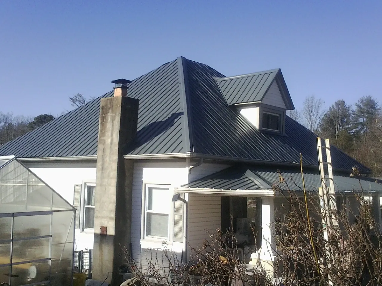 Dark blue standing seam metal roof on a white farmhouse with dormer — Slate & Tile Roof Repair by Roofing Brothers in Glen Wild