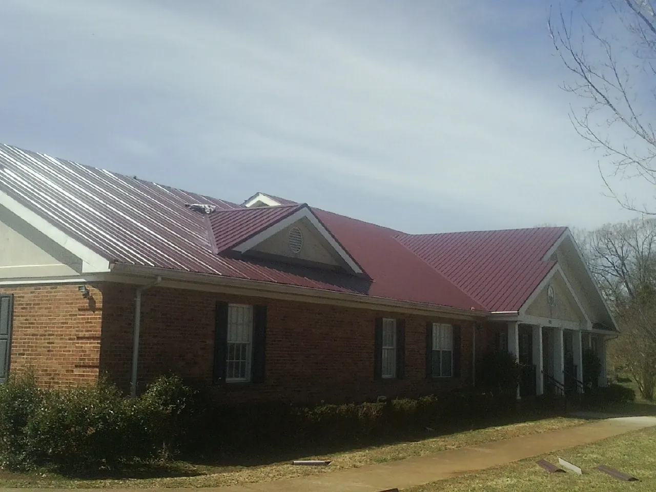 Red metal roof with gabled entries on a long brick building, from a Hail Damage Roof Repair job in Glen Wild