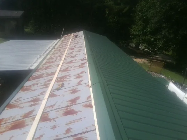 Old rusted panels beside newly installed green metal roofing — Wind Damage Roof Repair by Roofing Brothers in Glen Wild