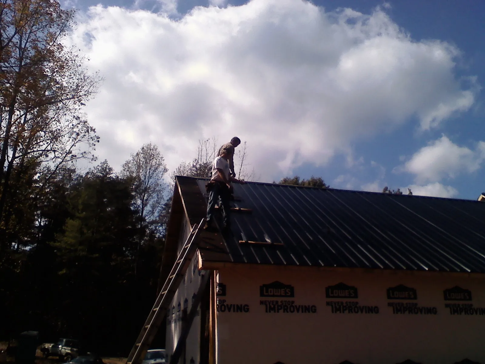 Roofer fastening dark metal panels high against a cloudy sky, from a Roof Inspection job in Glen Wild