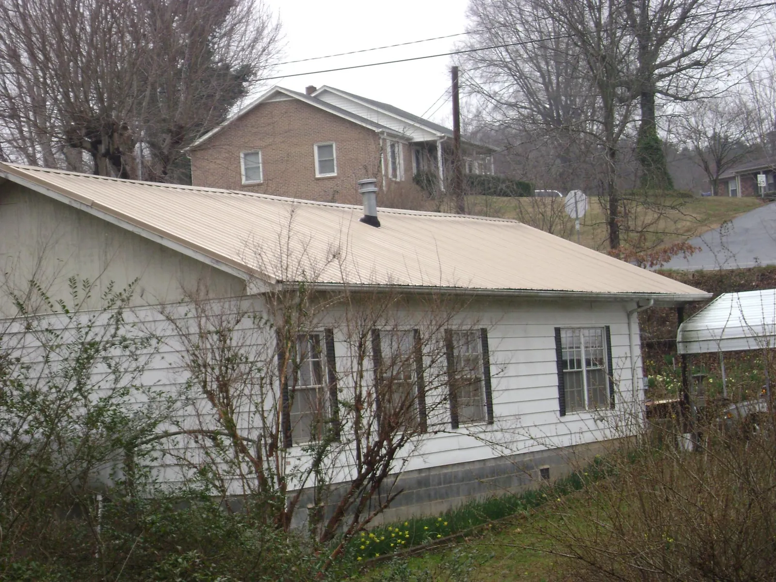 Tan metal roof on a white sided house set into a hillside — Commercial Roofing by Roofing Brothers in Glen Wild