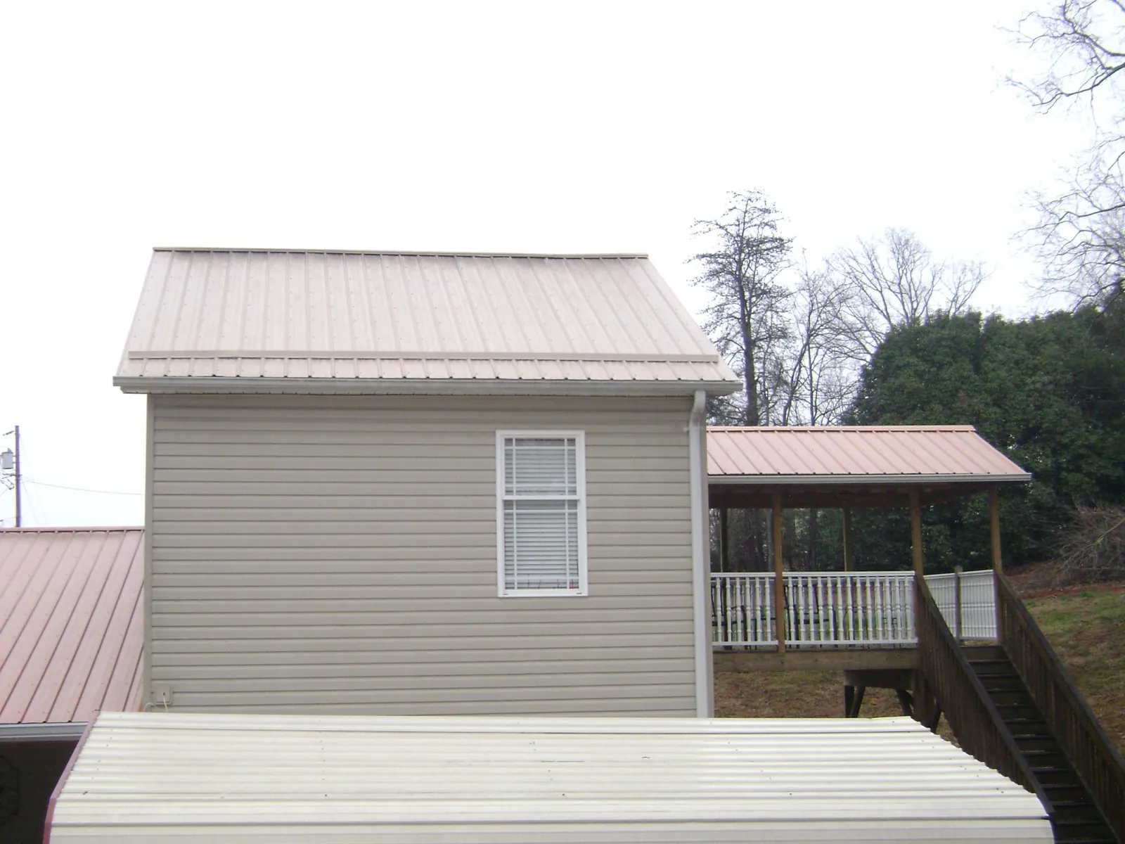 Tan metal roofs on a two story addition and attached porch, from a Roof Replacement job in Glen Wild
